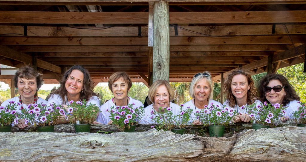 Laura (Riding) Jackson Foundation board members pose at the pole barn behind pots of purple flowers.